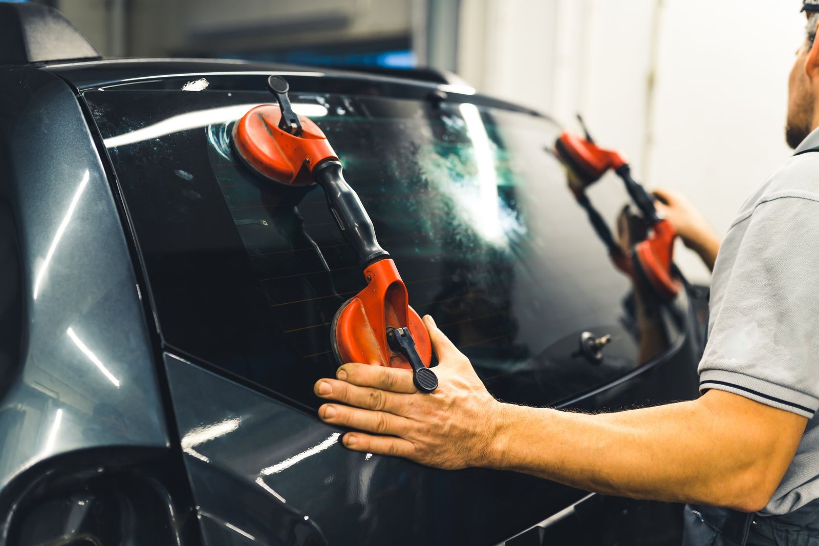 Technician installing a new rear windshield with suction cup tools
